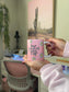 Person holding a pink mug with floral designs and text in a room with a desk and plant.