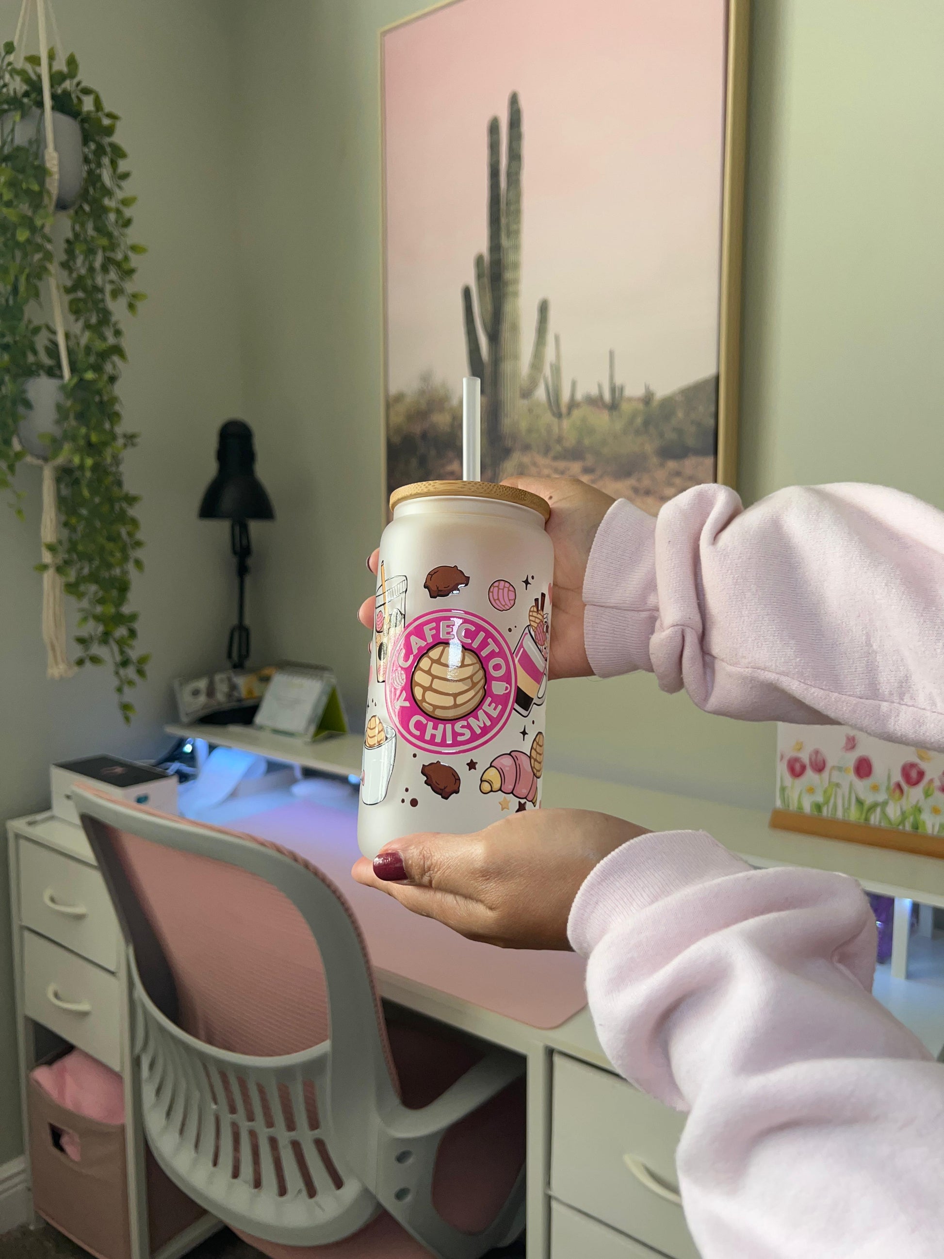 Person holding a pink cup with cartoon designs in a room with a desk and plants.