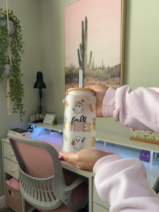 Person holding a 'fall vibes' cup in a room with a desk and plants.