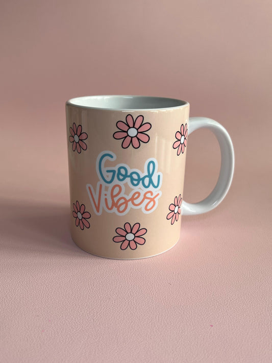 Beige mug with 'Good Vibes' text and flower designs on a pink background