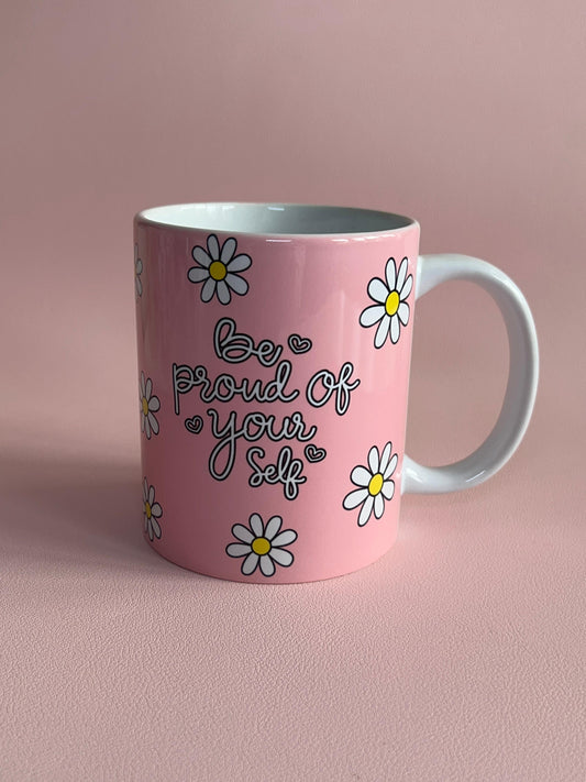 Pink mug with floral designs and 'Be proud of yourself' text on a pink background